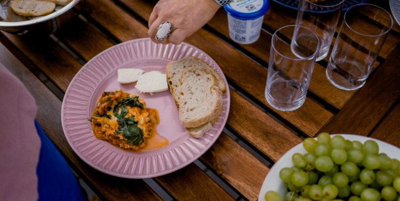 A casual outdoor dining table with bread, greens, and a side dish for brunch.