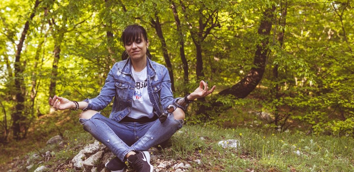 A woman meditates peacefully in a lush green forest, exuding calm and relaxation.